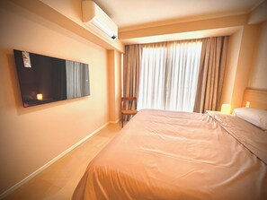 Ett hotellrum med en stor säng, en platt-TV som är monterad på väggen, en stol och ett fönster med gardiner.