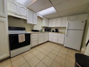 Une cuisine avec des meubles blancs, une cuisinière, un four à micro-ondes et un réfrigérateur.