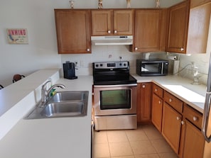 A kitchen with wooden cabinets, a stainless steel sink, a coffee maker, a microwave, and an oven.
