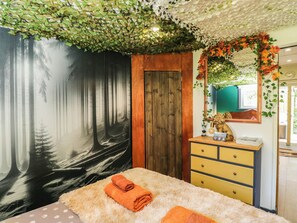 A room with a forest-themed mural, a wooden door, a yellow dresser, and a fluffy rug. - Squirrels Lodge (South Molton)