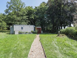 A rustic wooden shed with a red door, a gravel path leading to it, and a statue of a lion in the foreground. - Squirrels Lodge (South Molton)