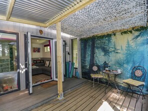 A covered outdoor area with a wooden deck, a mural of a forest scene, and a seating area with a table and chairs. - Squirrels Lodge (South Molton)
