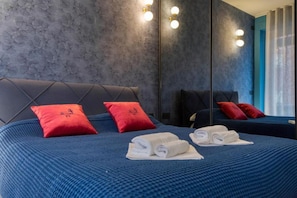 Une chambre d’hôtel avec un grand lit, deux oreillers rouges, un miroir et un mur bleu à texture.