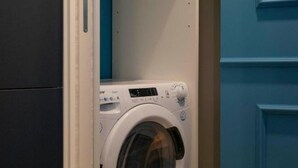 A compact, modern washing machine in a room with blue walls and a white door. - VivimiHome-Luxury Suite: Acquamarina (Milan)
