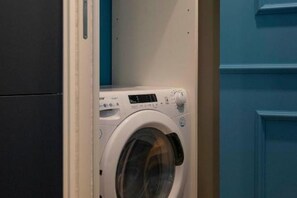 Eine kompakte, moderne Waschmaschine in einem Raum mit blauen Wänden und einer weißen Tür.