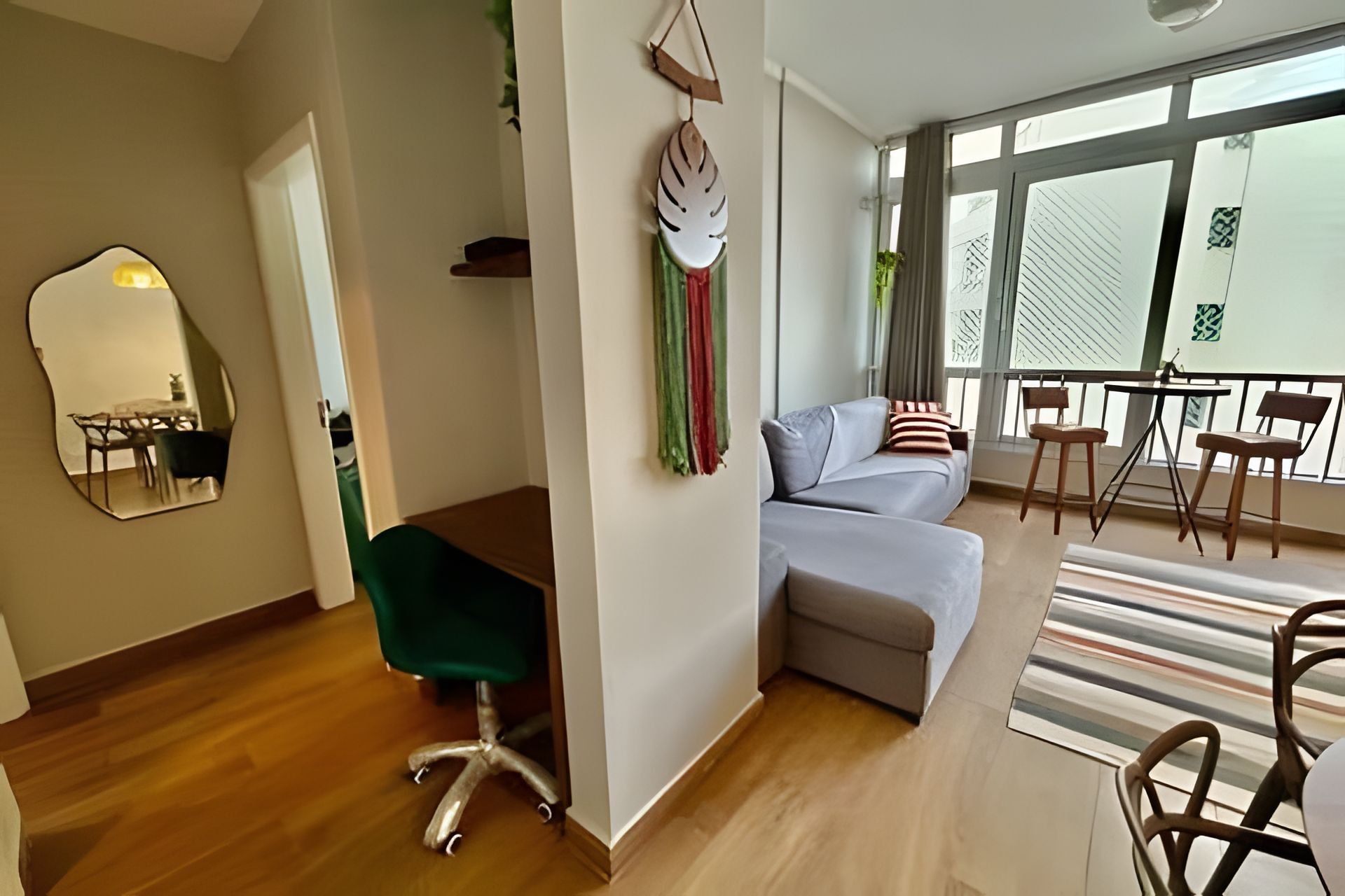 Een moderne woonkamer met een bank, een eethoek met stoelen, een spiegel en een balkon met een balustrade.