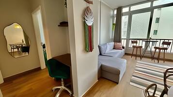 A modern living room with a sofa, a dining area with chairs, a mirror, and a balcony with a railing.
