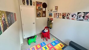 Un pasillo con una puerta, un caballo de juguete verde, una silla roja y un tapete de juego con el alfabeto en varios colores.