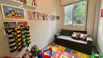 Un cuarto de juegos infantil con un sofá, alfombras de espuma con el abecedario y varios juguetes.