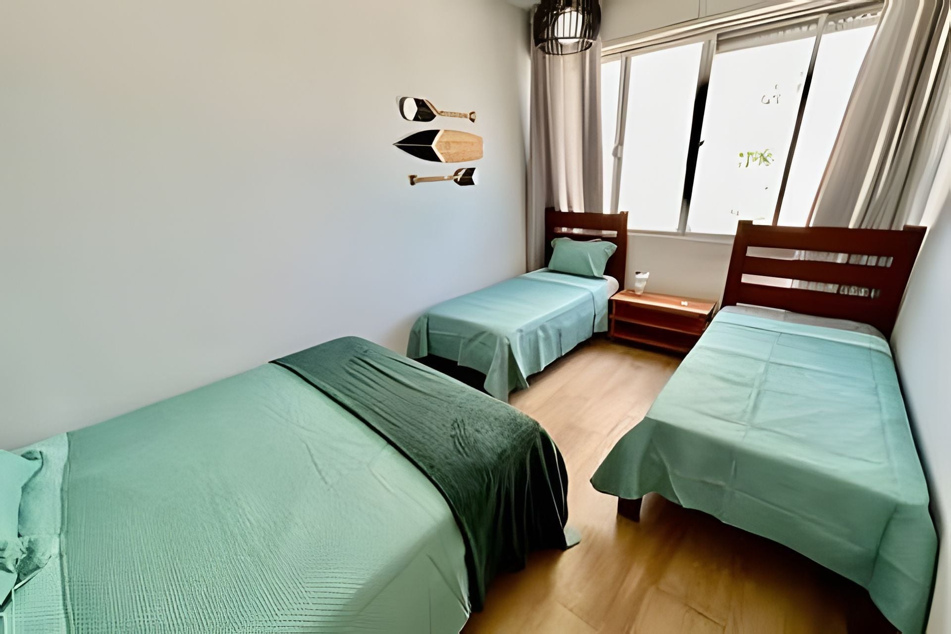 Una habitación con dos camas individuales, cabecera de madera, una mesita y una ventana con cortinas.