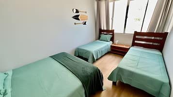 Una habitación con dos camas individuales, cabecera de madera, una mesita y una ventana con cortinas.