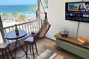 Ein Zimmer mit Meerblick, einer Hängematte, einem Fernseher und einem kleinen Tisch mit einer Flasche.
