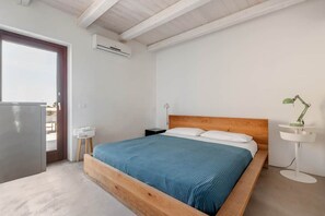 A bedroom with a wooden bed, a bedside table, a lamp, and a view through a door.