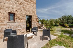 Un bâtiment en pierre doté d’un patio aménagé avec du mobilier d’extérieur et d’un escalier menant à l’entrée.