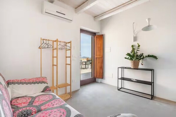 A room with a sofa, a wooden coat rack, a potted plant, and a black console table.