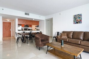 A modern living room with a brown leather sofa, a wooden coffee table, and a dining area with a brown chair and a dining table. - 2 Penthouses Sleeps 14 · Brickell, Free Parking (Miami)
