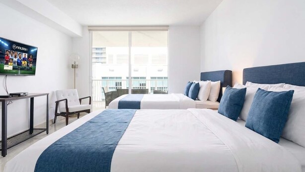 Une chambre d’hôtel avec deux lits, un téléviseur fixé au mur, un bureau et une chaise.