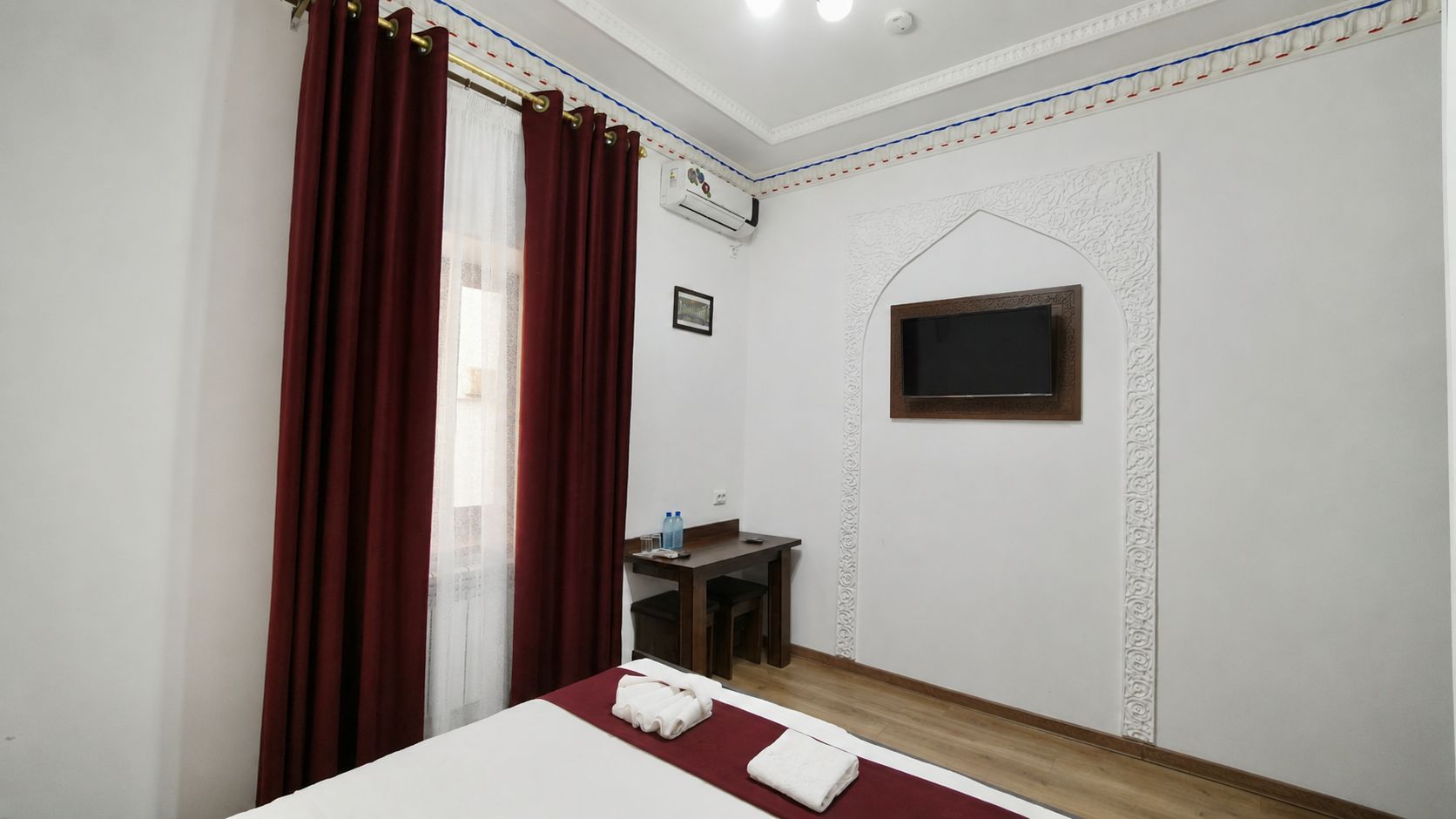 Una habitación de hotel con cama, una mesita, un televisor y una ventana con cortinas.