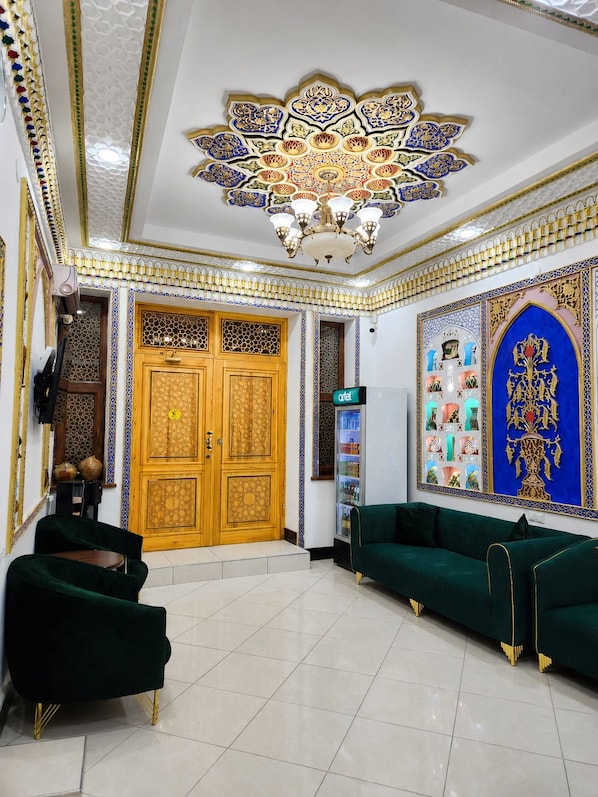 Un vestíbulo de hotel con diseño tradicional, que presenta una puerta de madera grande, un sofá verde y un techo decorativo.