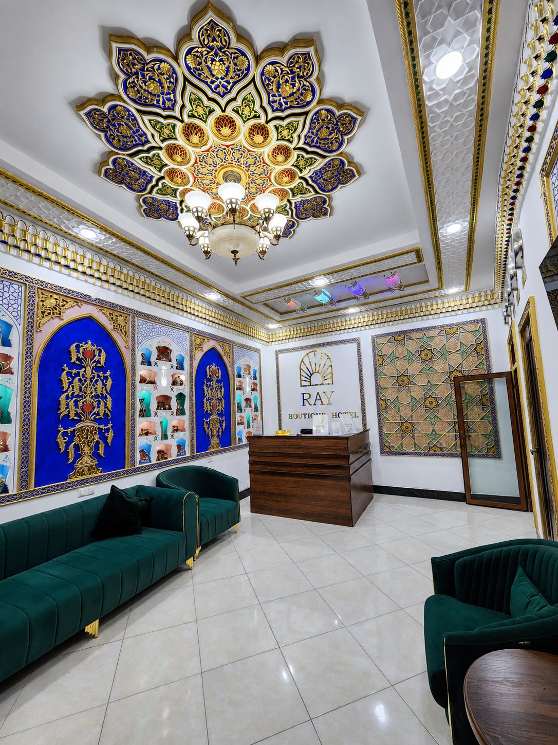 Un hall d’hôtel avec un comptoir d’accueil, des canapés verts et des décorations murales complexes.