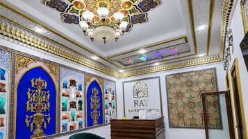 Un hall d’hôtel avec un comptoir d’accueil, des canapés verts et des décorations murales complexes.