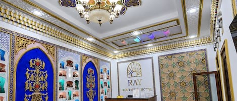 A hotel lobby with a reception desk, green sofas, and intricate wall decorations.