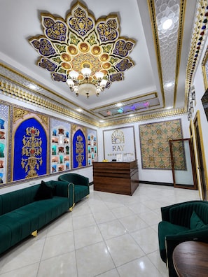A hotel lobby with a reception desk, green sofas, and intricate wall decorations. - RAY BOUTIQUE HOTEL (Bukhara)