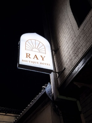 Un letrero de hotel con el nombre 'RAY BOUTIQUE HOTEL' y un logo con forma de sol.