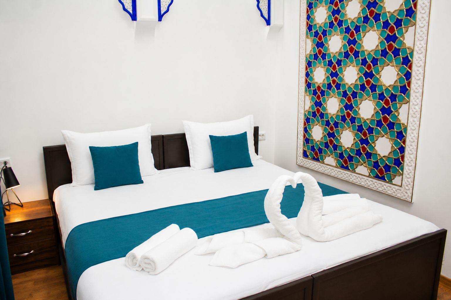 Un lit bien fait, avec une literie blanche et turquoise, un élément décoratif mural et une serviette pliée posée sur le lit.
