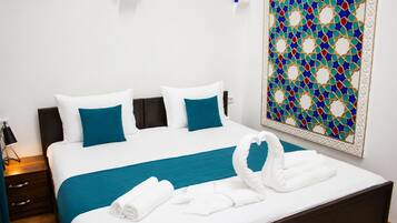 Un lit bien fait, avec une literie blanche et turquoise, un élément décoratif mural et une serviette pliée posée sur le lit.