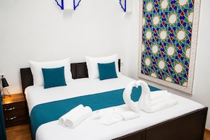 A neatly made bed with white and teal bedding, a decorative wall piece, and a folded towel on the bed. - RAY BOUTIQUE HOTEL (Bukhara)