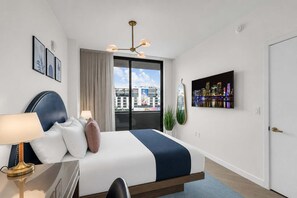 A hotel room with a bed, a desk, a lamp, a cityscape view, and a mounted artwork. - 2 Units on One Floor for 8 · Wynwood Rooftop Pool (Miami)