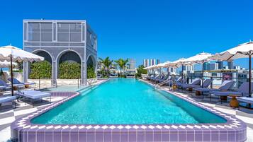 Une piscine entourée de chaises longues et de parasols, le tout bordé d’un bâtiment moderne aux fenêtres en arc de cercle.