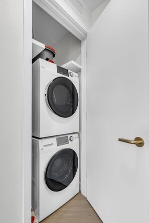A laundry room with two stacked front-loading washing machines and a door with a brass handle. - 2 Units on One Floor for 8 · Wynwood Rooftop Pool (Miami)