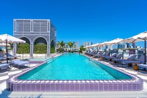 A swimming pool with lounge chairs and umbrellas, surrounded by a modern building with arched windows. - Wynwood 2-Unit Combo for 8 · Same Floor + Rooftop (Miami)