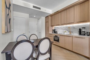 A modern kitchen with wooden cabinets, a marble countertop, and a dining area with a dark wooden table and upholstered chairs. - Wynwood 2-Unit Combo for 8 · Same Floor + Rooftop (Miami)