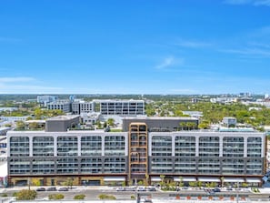 A modern multi-story building with a central atrium, surrounded by a parking lot and a clear sky. - Wynwood 2-Unit Combo for 8 · Same Floor + Rooftop (Miami)
