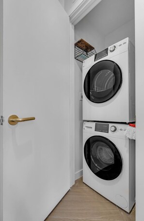 A laundry room with two stacked front-loading washing machines and a wooden door. - Wynwood 2-Unit Combo for 8 · Same Floor + Rooftop (Miami)