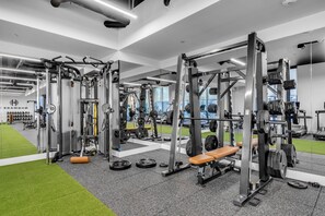 A gym with various weightlifting equipment, a green artificial turf area, and a bench. - 2 Apts for 8 · 2BR/2BA, Rooftop Pool, Downtown MIA (Miami)