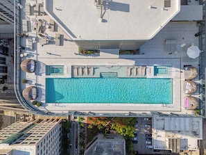 An aerial view of a rooftop swimming pool with lounge chairs and umbrellas, surrounded by buildings. - 2 Apts for 8 · 2BR/2BA, Rooftop Pool, Downtown MIA (Miami)