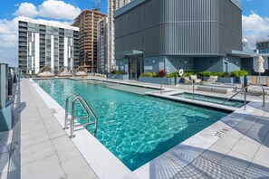 A modern hotel with a rooftop pool, a large building with a sign indicating rental prices, and a view of other high-rise buildings. - 2 Apts for 8 · 2BR/2BA, Rooftop Pool, Downtown MIA (Miami)