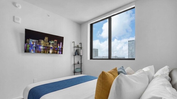 Moderni hotellihuone, jossa on suuri sänky, näkymä kaupunkiin ja ikkuna, josta avautuu panoraamanäkymä kaupungin siluettiin.