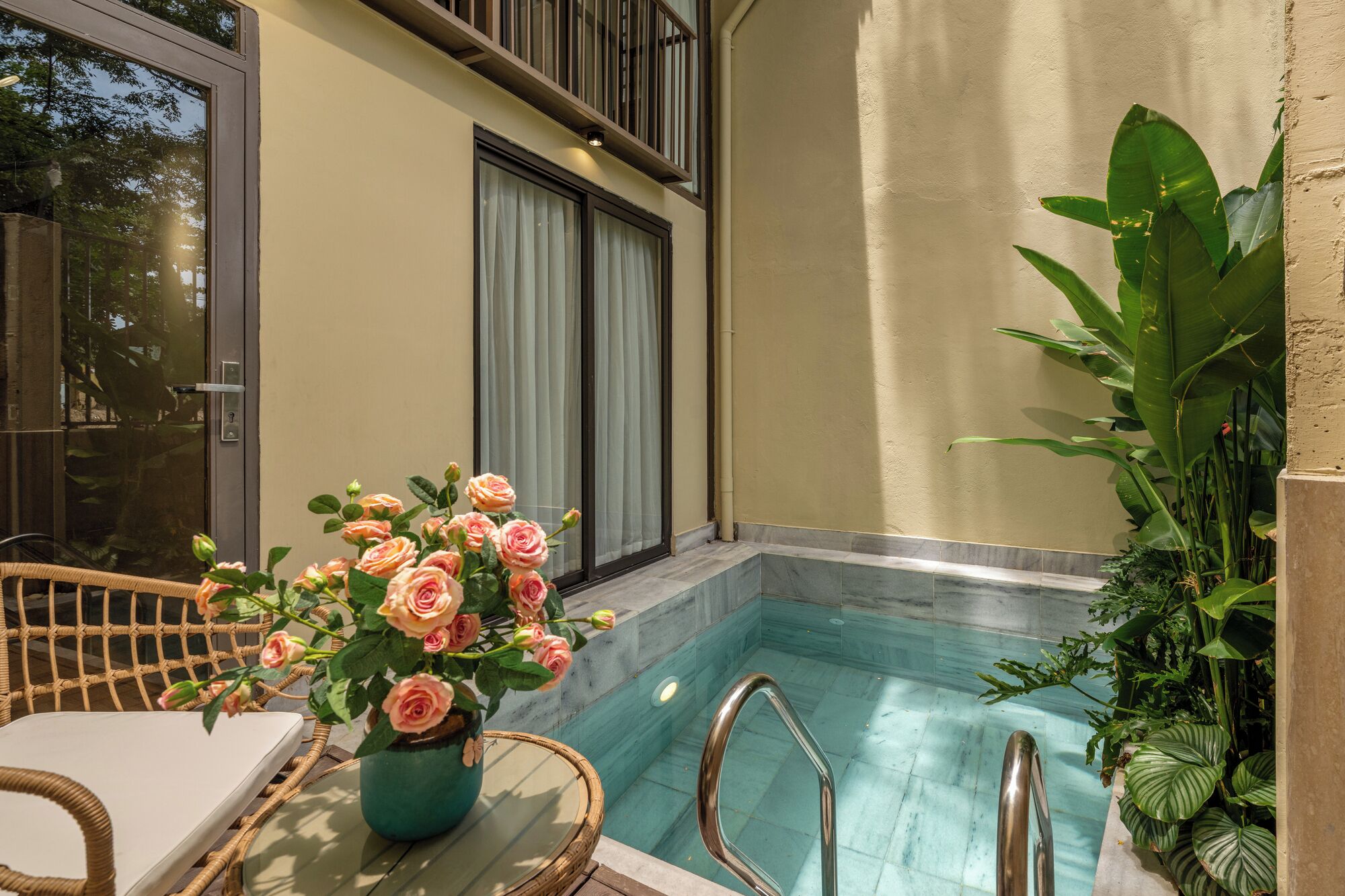 A pool area with a wicker chair, a vase of flowers, and a staircase leading to a balcony.