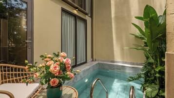 A pool area with a wicker chair, a vase of flowers, and a staircase leading to a balcony.