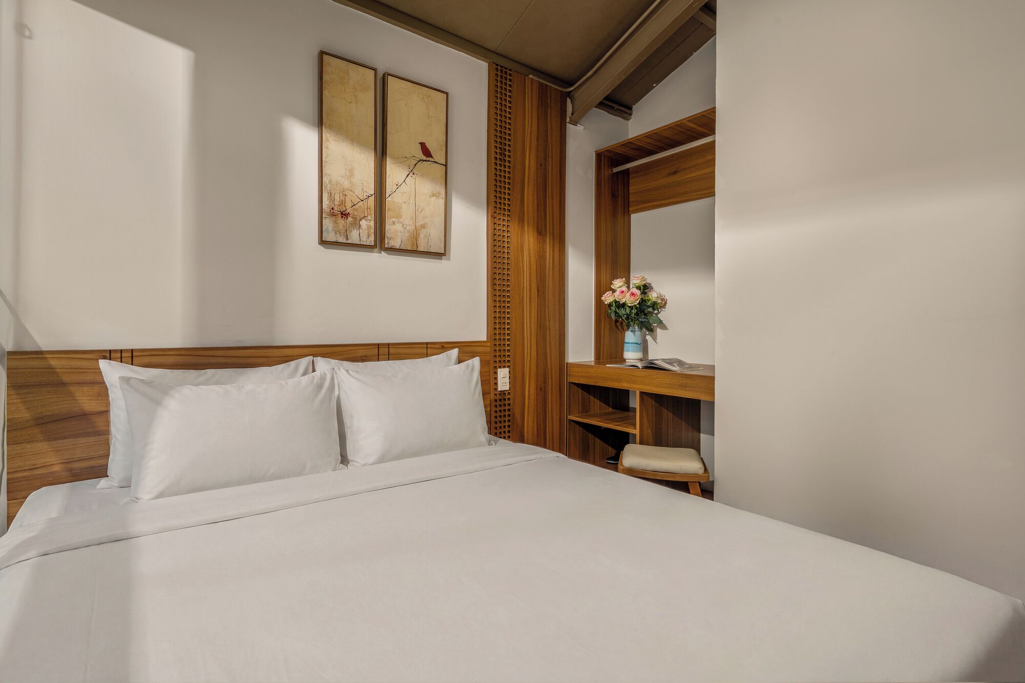 A neatly made bed with white linens, a wooden headboard, and a nightstand with a vase of flowers.