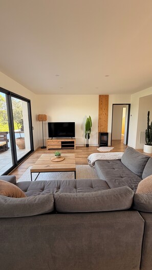 A modern living room with a large grey sofa, a flat-screen TV, a wooden coffee table, and a potted plant. - A peaceful retreat with a pool and a view of the countryside (Preignan)