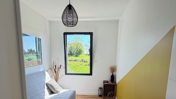 Ein Schlafzimmer mit Bett, Fenster, einer Pendelleuchte und Holzboden.