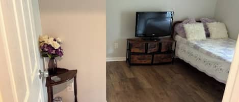 Een slaapkamer met een bed, een televisie op een houten standaard en een klein tafeltje met een bloevas.