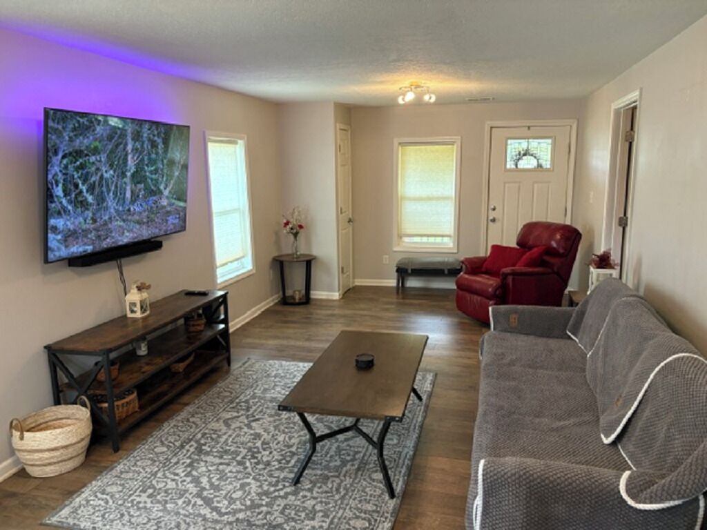 A living room with a flat-screen TV, a sofa, a coffee table, and a patterned rug.