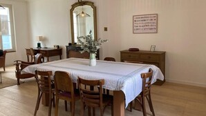 A dining room with a table set for six, surrounded by wooden chairs. A vase with greenery is placed on the table.
